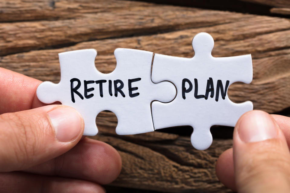 Closeup of hands holding retire plan matching jigsaw pieces against wood