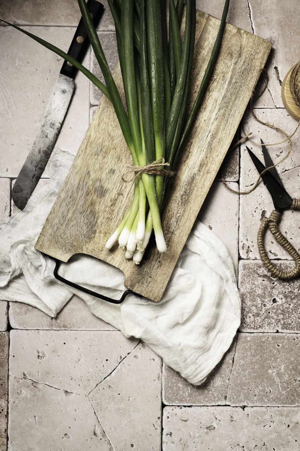 fresh spring onions on rustic wooden board with knife and scissors