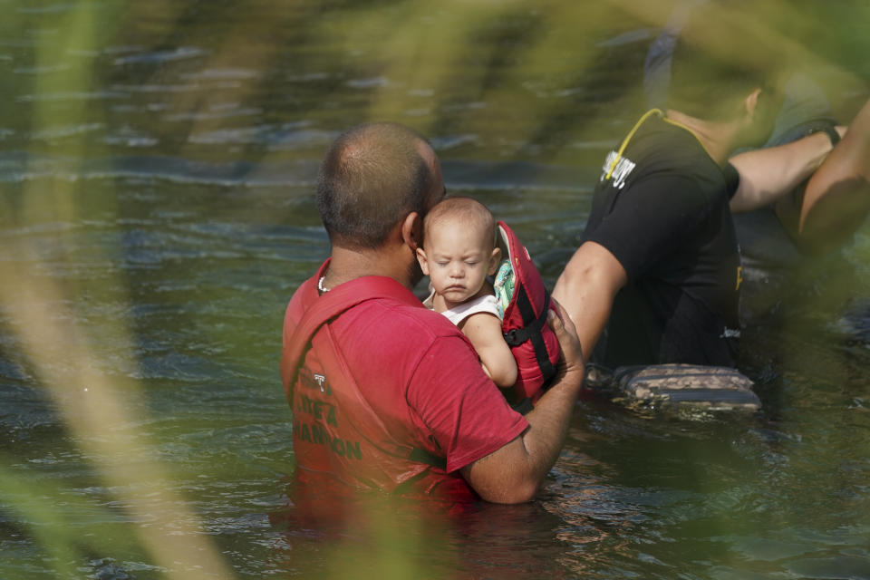 A migrant crosses the Rio Grande river with a child in arms, as seen from Matamoros, Mexico, Wednesday, May 10, 2023. The U.S. on May 11 will begin denying asylum to migrants who show up at the U.S.-Mexico border without first applying online or seeking protection in a country they passed through, according to a new rule released on May 10. (AP Photo/Fernando Llano)