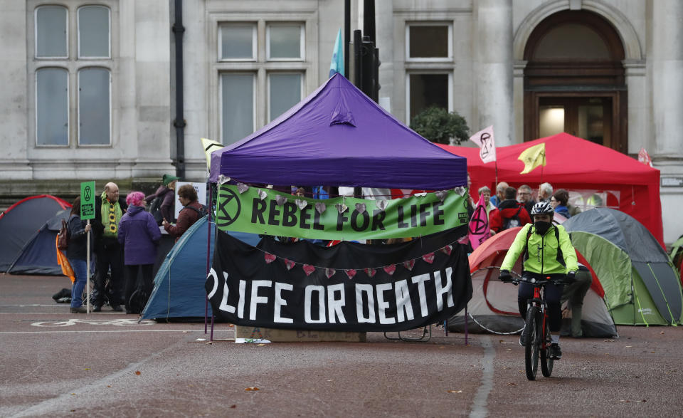 A commuter cycles past climate change protesters at Horseguards in London, Tuesday, Oct. 8, 2019. Police are reporting they have arrested more than 300 people at the start of two weeks of protests as the Extinction Rebellion group attempts to draw attention to global warming. (AP Photo/Alastair Grant)
