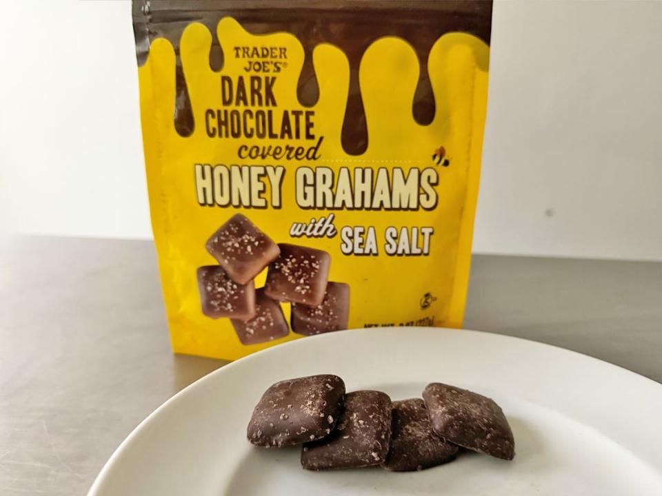Yellow bag of Trader Joe's dark-chocolate-covered honey grahams with sea salt with a plate of square-shaped chocolate grahams in front