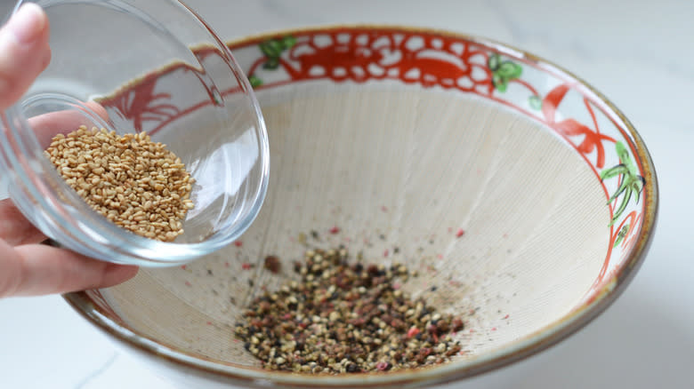 Adding sesame seeds to crushed peppercorns
