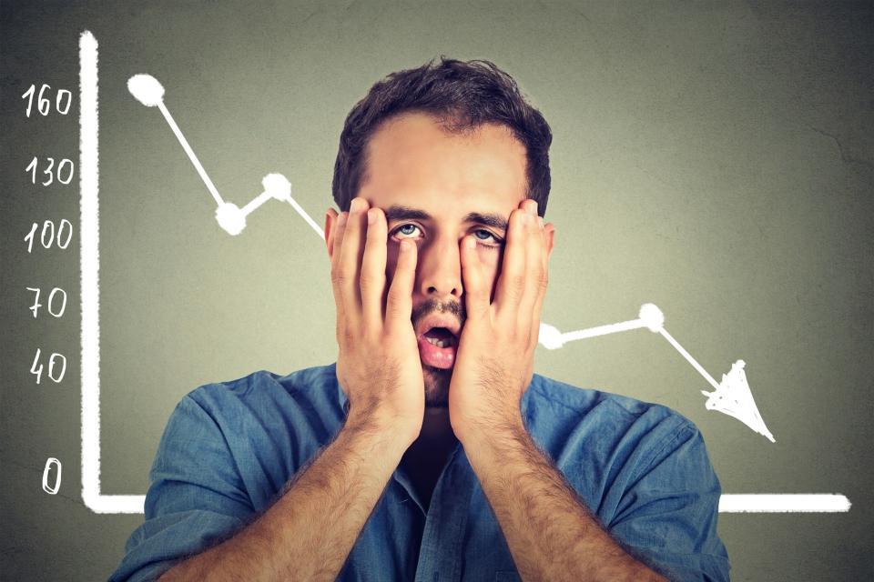 A man standing in front of a chart with a down arrow. He has put his hands to his face and squished them together a bit.