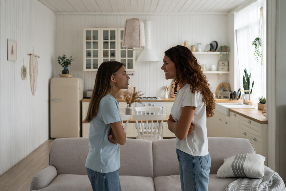 Mother and daughter standing face to face, smiling, having a conversation in a home kitchen