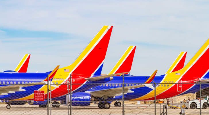 An image of two blue, yellow, and red Southwest planes with machines in the background and a barbed wire fence in front.