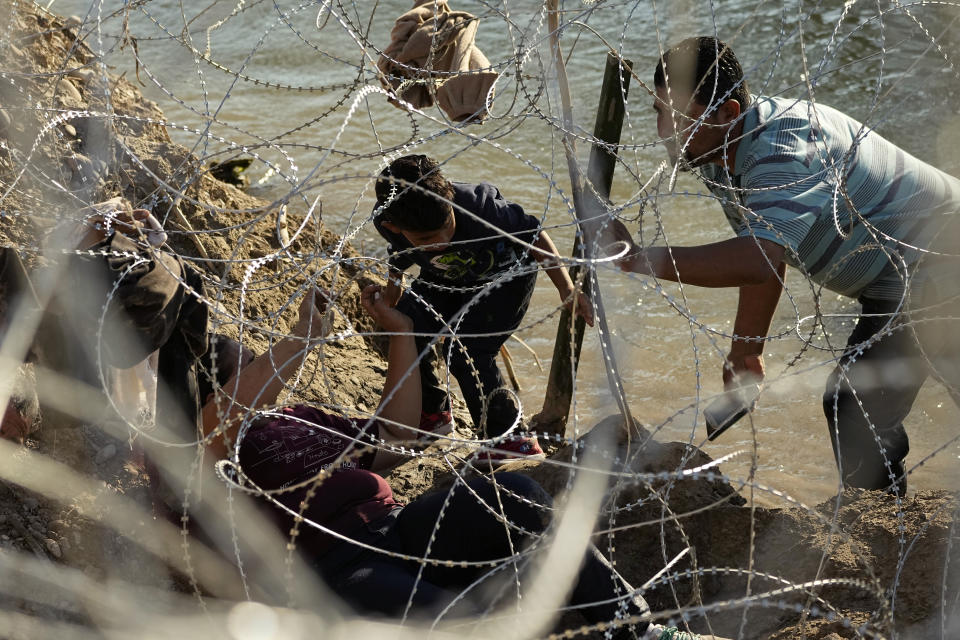 Migrants who crossed the Rio Grande from Mexico to the U.S. work their way through concertina wire, Friday, Sept. 22, 2023, in Eagle Pass, Texas. (AP Photo/Eric Gay)