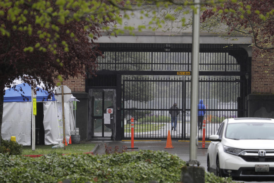 In this April 22, 2020, photo, people walk on the other side of a gate at Western State Hospital in Lakewood, Wash., where a sign tells employees that they must be medically screened at one of two other buildings before entering. Employees at the facility — the state's largest psychiatric hospital — say that problems with testing for the coronavirus likely produced inaccurate results and exposed them to the virus a second time. (AP Photo/Ted S. Warren)