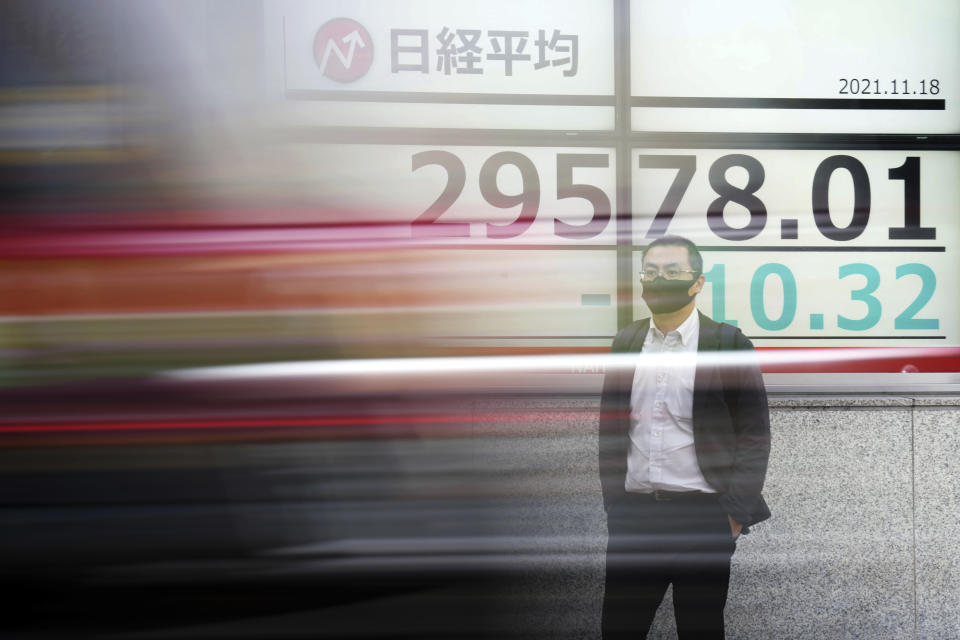 As a car passes by, a man wearing a protective mask stands near an electronic stock board showing Japan's Nikkei 225 index at a securities firm Thursday, Nov. 18, 2021, in Tokyo. Asian shares mostly declined Thursday after stock indexes shuffled lower on Wall Street. (AP Photo/Eugene Hoshiko)