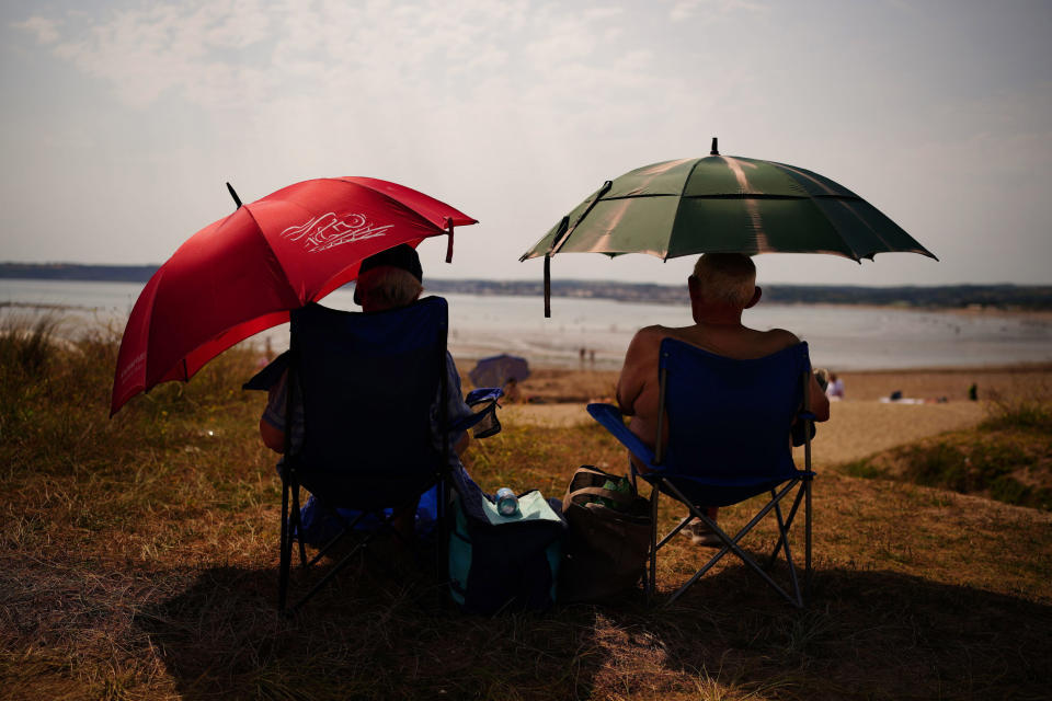 People sheltering under umbrellas from the sun in St Michael's Bay in Cornwall, England, Sunday July 17, 2022. The Met office has issued its first-ever “red warning” of extreme heat for Monday and Tuesday, when temperatures in southern England may reach 40 C (104 F) for the first time. (Ben Birchall/PA via AP)