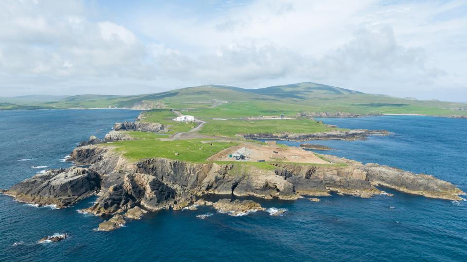 overhead view of a rugged island. cliffs are set against the quiet ocean. the sky with clouds is overhead