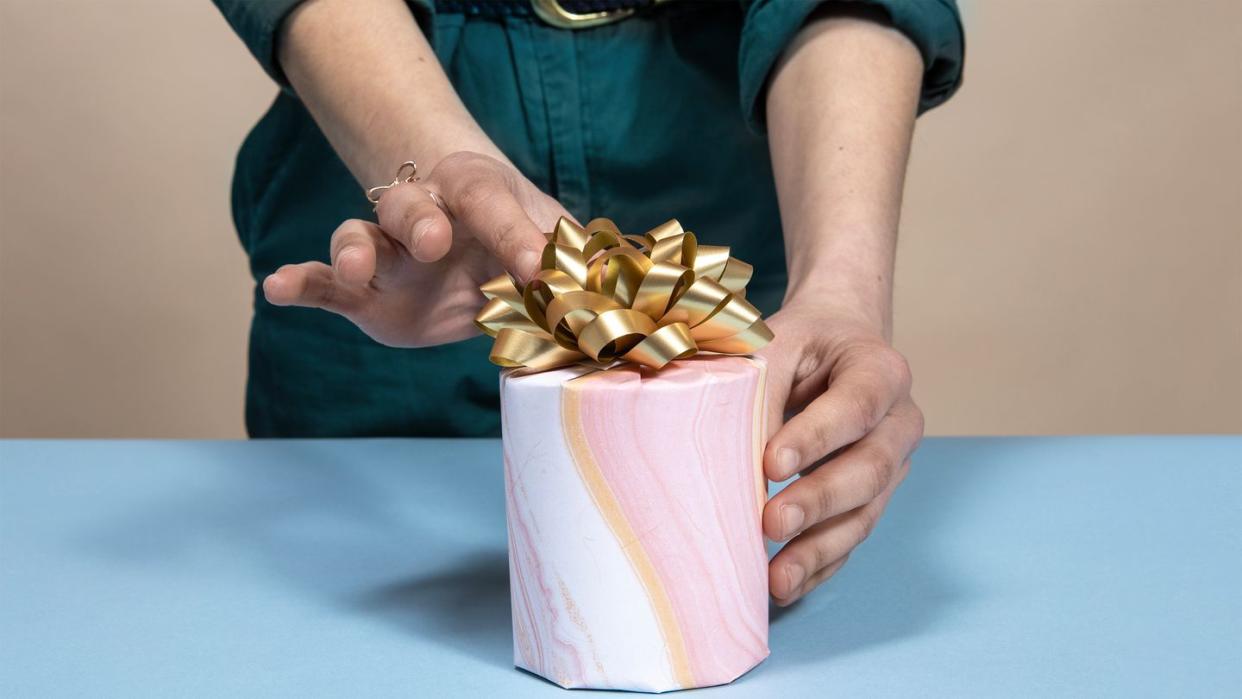 hands adjusting gold bow on gift wrapped candle