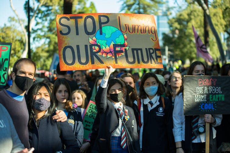 A group of young people in school uniforms with a handpainted sign reading 'Stop burning our future'/