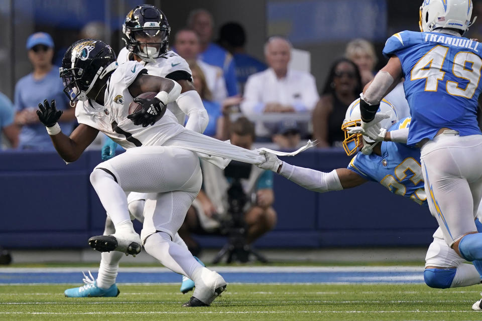 Jacksonville Jaguars running back Travis Etienne Jr. (1) runs as Los Angeles Chargers cornerback Bryce Callahan (23) grabs his jersey during the second half of an NFL football game in Inglewood, Calif., Sunday, Sept. 25, 2022. (AP Photo/Mark J. Terrill)