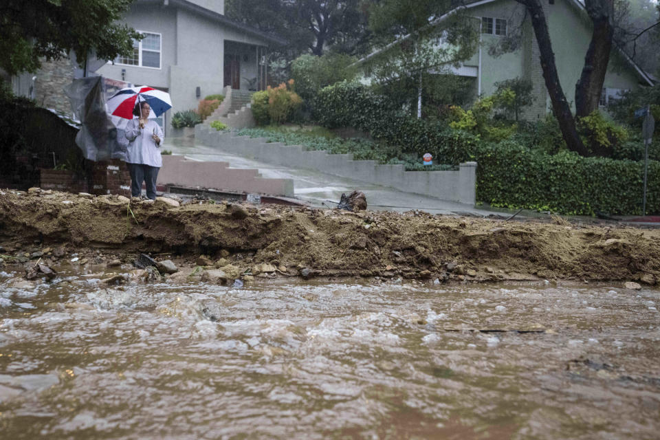 A resident keeps watch on Fredonia Drive in Studio City, Calif., where a mudslide is blocking the road during a rain on Tuesday, Jan. 10, 2023. California saw little relief from drenching rains as the latest in a relentless string of storms swamped roads, turned rivers into gushing flood zones and forced thousands of people to flee from towns with histories of deadly mudslides.(Sarah Reingewirtz /The Orange County Register via AP)