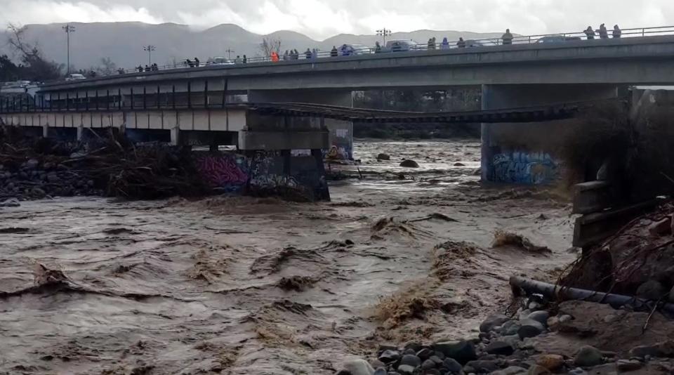 Water rushes under a collapsed train bridge over the Sespe Creek in Fillmore as onlookers snap photos from Old Telegraph Road Tuesday in this still from a video.