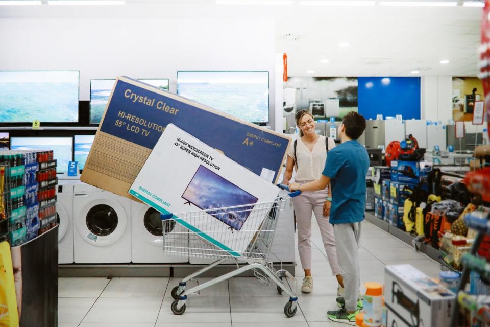 A woman and young man at an electronics store with two large TVs in their shopping cart.