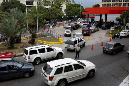 A police officer controls the traffic as people wait in line to fill the tanks of their cars at a gas station of the state oil company PDVSA in Caracas, Venezuela March 23, 2017. REUTERS/Carlos Garcia Rawlins