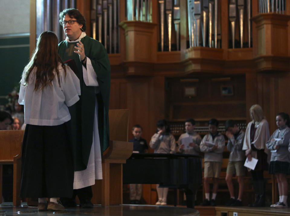 In this Feb. 7, 2020, photo, Natalie Kricken, student at St. Rita Catholic School, left, holds the Bible in front of converted Catholic Priest Joshua Whitfield during a weekly student Mass at St. Rita Catholic Community in Dallas. Whitfield came to the Catholic church as a former Episcopalian pastor, a husband and soon-to-be dad. (AP Photo/Jessie Wardarski)