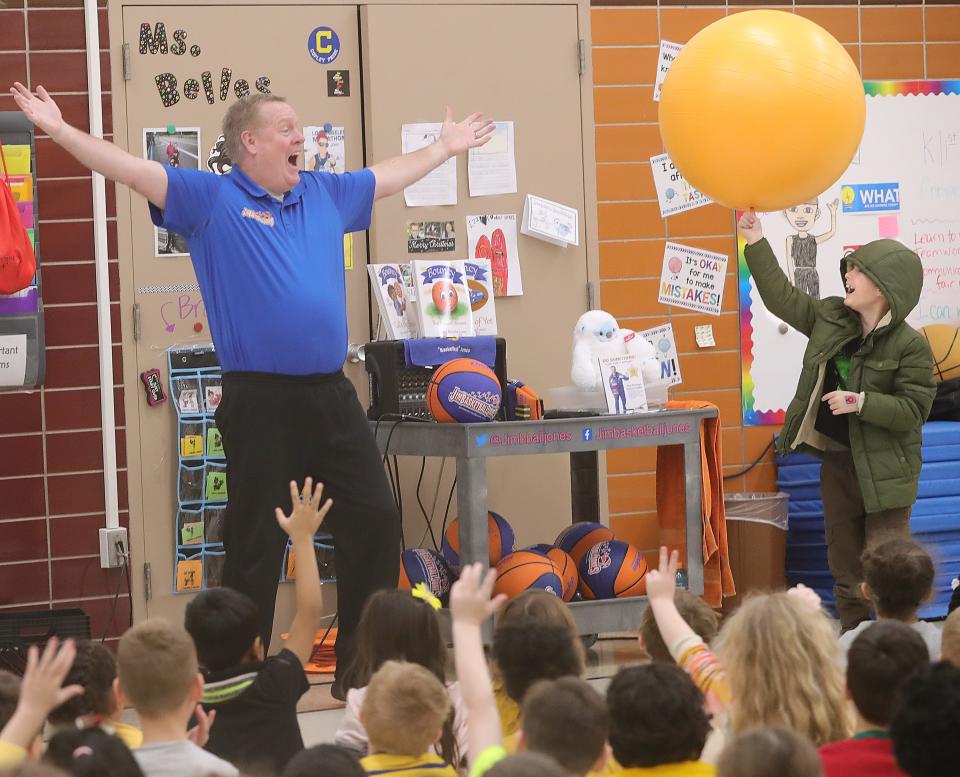 Jim "Basketball" Jones gets help balancing a spinning ball on the finger of Hunter Swisher during his performance at Herberich Primary School on Tuesday in Fairlawn.