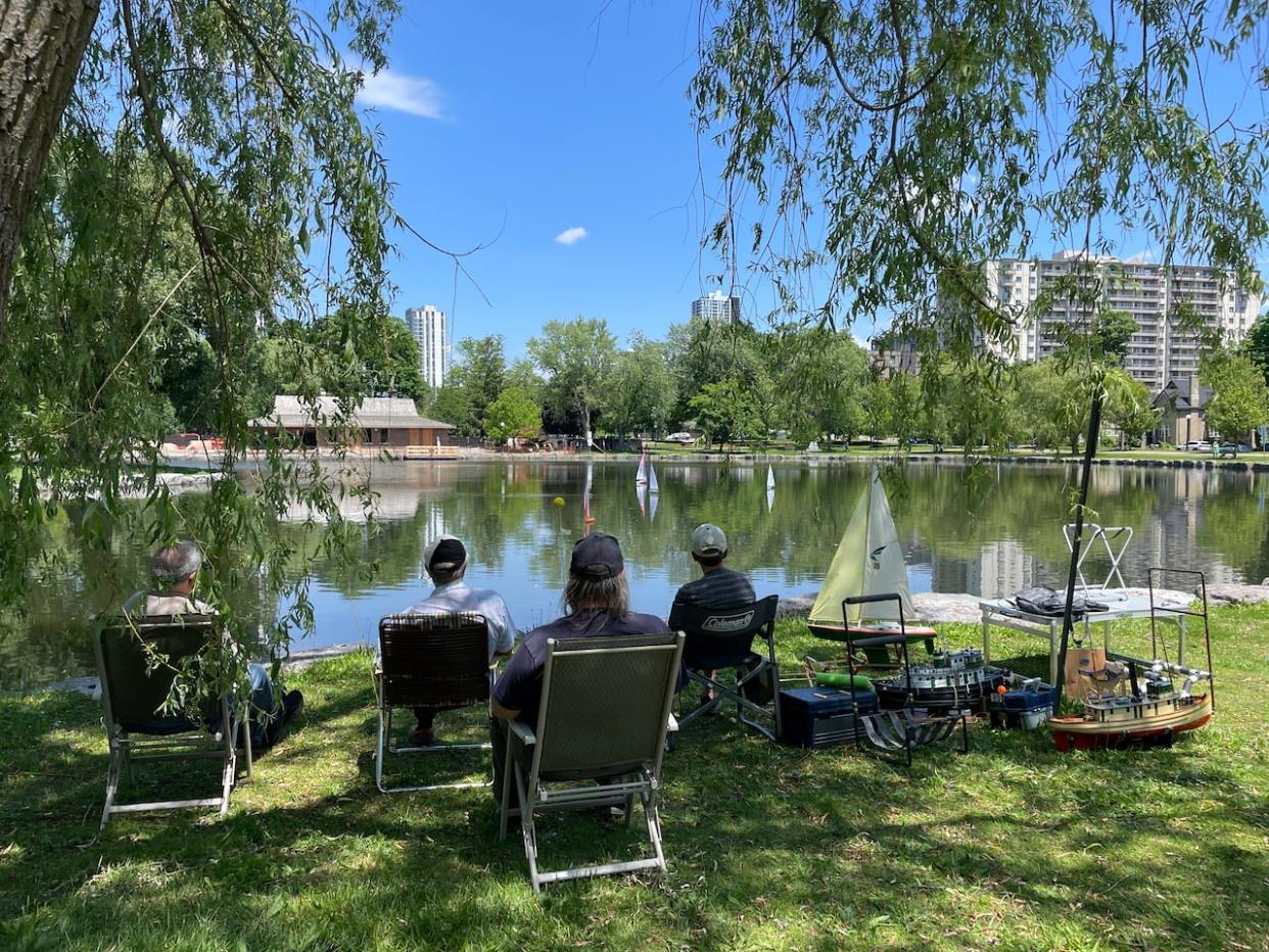 A group of people use remote control boats on the water in Kitchener's Victoria Park last Wednesday. A shady spot will be a good place to be this week as temperatures are set to soar to 30 C and higher. (Kate Bueckert/CBC - image credit)