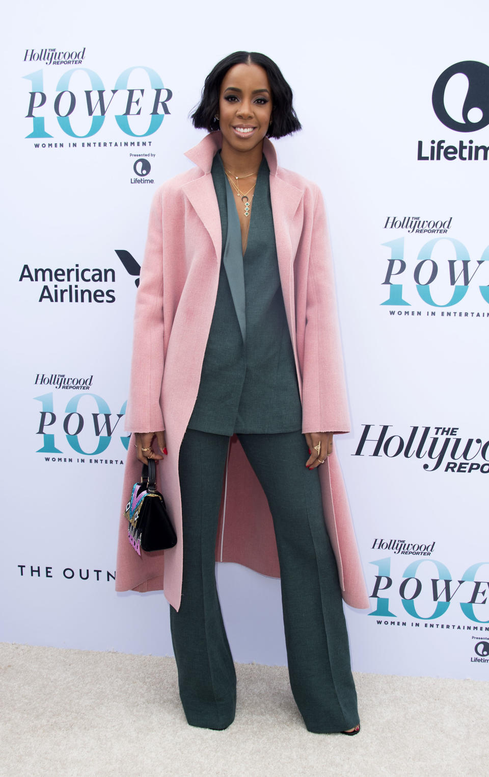Recording artist Kelly Rowland attends the Hollywood Reporter's 25th Annual Women In Entertainment Breakfast. She wears a dark green suit with a pink coat over the top.