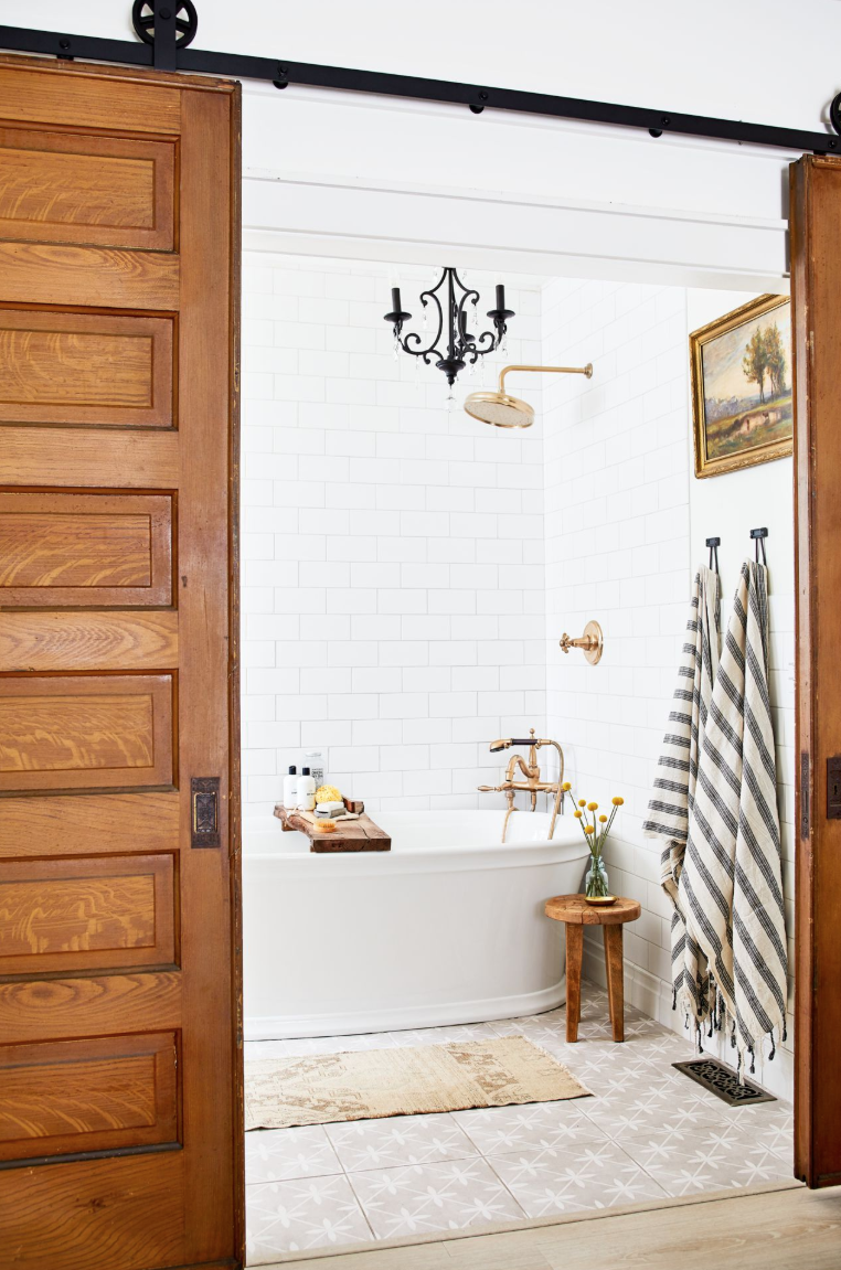 white bathroom with sliding barn doors, taupe floor tiles with geometric dragonfly design, freestanding tub, subway wall tile