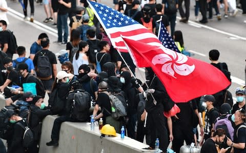 A man waves a US and Hong Kong flag while standing on a divider after he and other protesters occupied Harcourt Road while marching against a controversial extradition bill in Hong Kong on July 21, 2019. - Credit: afp