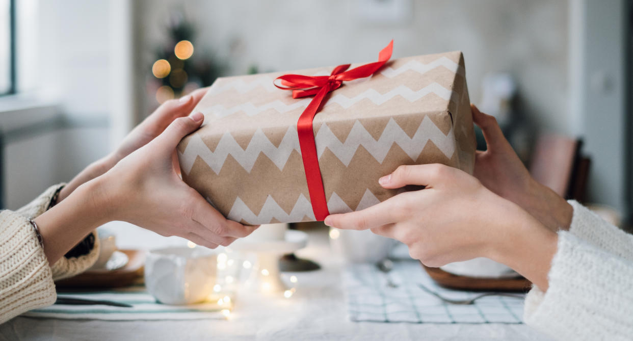 People sit at a table and pass a Christmas present between them. (Getty Images)