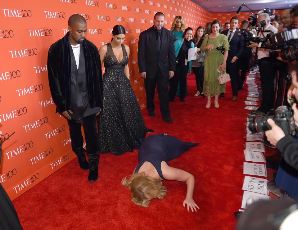 Amy Schumer lays on the ground on the red carpet in front of Kim Kardashian and Kanye West