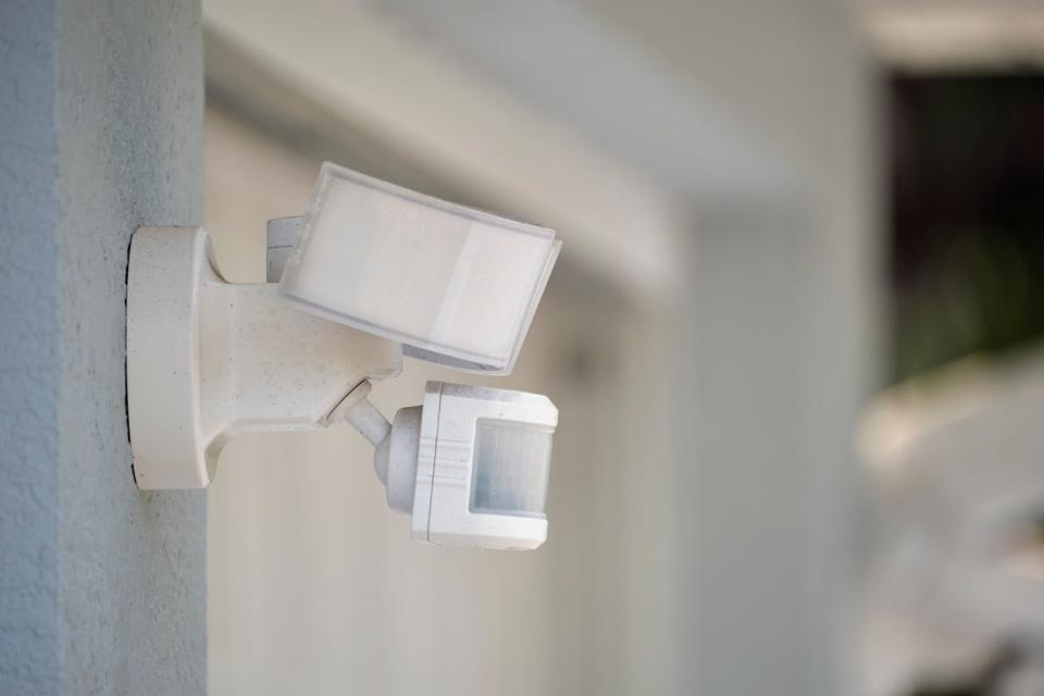 Motion sensor with light detector mounted on exterior wall of private house as part of security system.