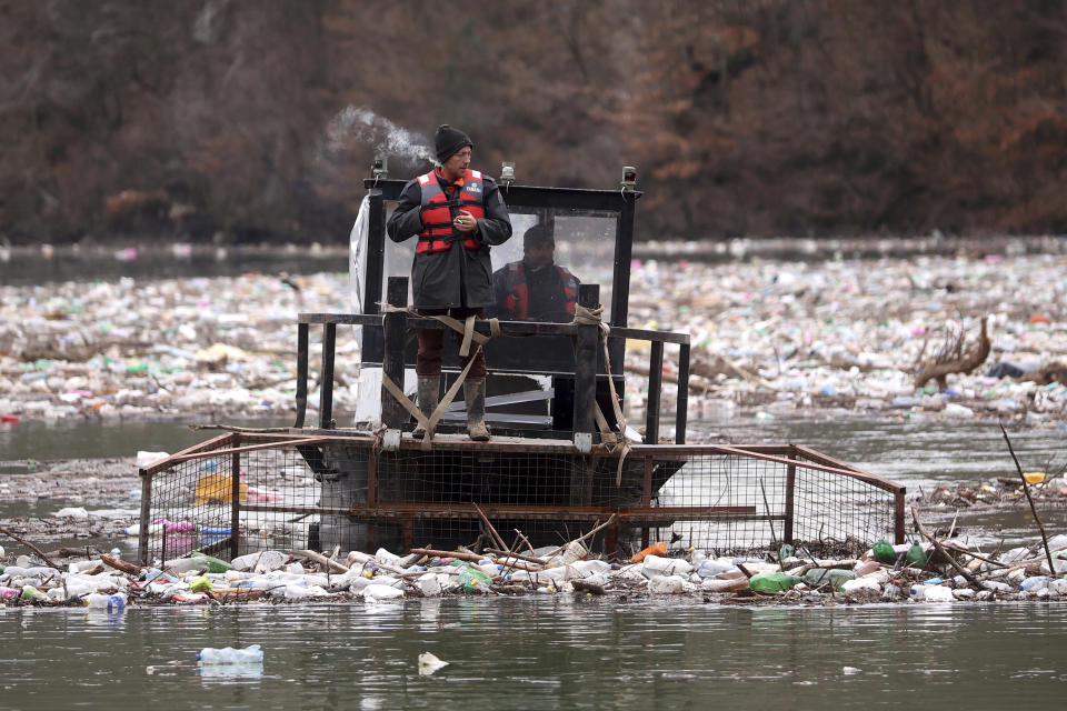 Utility company workers push the waste to the shore of Lim river near Priboj, Serbia, Monday, Jan. 30, 2023. Plastic bottles, wooden planks, rusty barrels and other garbage dumped in poorly regulated riverside landfills or directly into the rivers accumulated during high water season, behind a trash barrier in the Lim river in southwestern Serbia. (AP Photo/Armin Durgut)