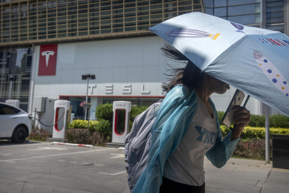 A woman carrying an umbrella walks past an electric vehicle charging station outside of a Tesla dealership in Beijing, Saturday, June 24, 2023. Threatened by possible shortages of lithium for electric car batteries, automakers are racing to lock in supplies of the once-obscure "white gold" in a politically and environmentally fraught competition from China to Nevada to Chile. (AP Photo/Mark Schiefelbein)
