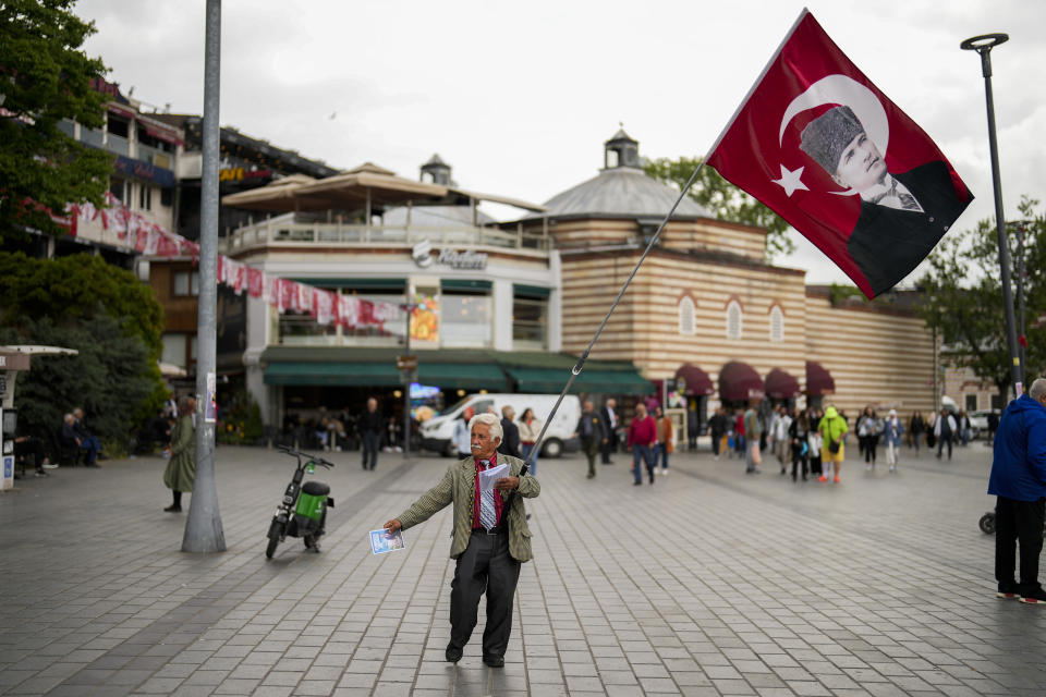 A supporter of People pass by the poster of Republican People's Party Presidential candidate Kemal Kilicdaroglu gives election handouts in Istanbul, Turkey, Tuesday, May 23, 2023. Two opposing visions for Turkey’s future are on the ballot when voters return to the polls Sunday for a runoff presidential election, which will decide between an increasingly authoritarian incumbent President Recep Tayyip Erdogan and challenger Kemal Kilicdaroglu, who has pledged to restore democracy. (AP Photo/Francisco Seco)