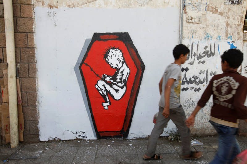 Boys walks pass a graffiti of artist Murad Subai depicting a child suffering from malnutrition in a coffin along a street in Sanaa, Yemen, October 20, 2016. REUTERS/Mohamed al-Sayaghi