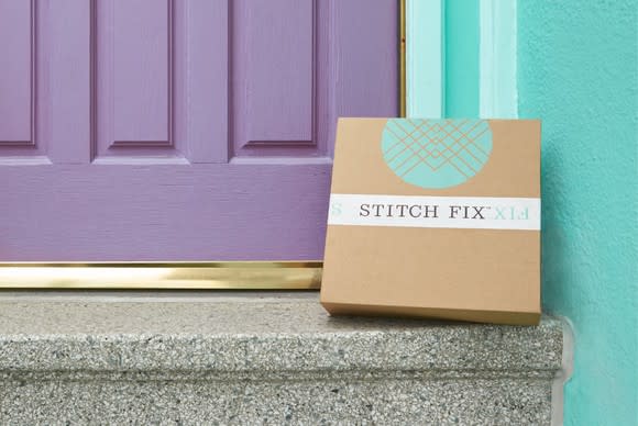 Stitch Fix box on a step in front of a purple door of a teal blue house that happens to match the color of the logo on the box.