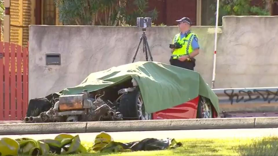 A police officer with a camera stands next to the remains of a red Ferrari after a fatal car crash in Perth.