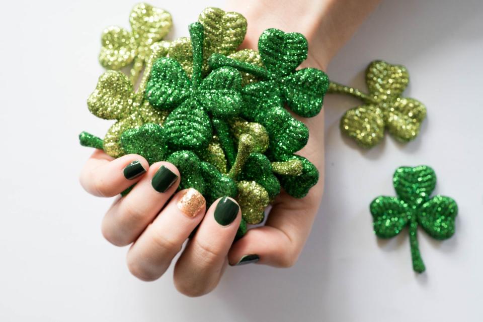 a person with a green and gold manicure holding a glittery clovers for st patricks day