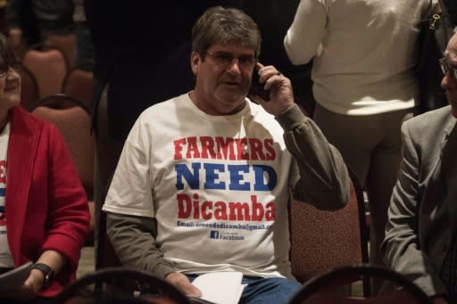 A farmer wearing a T-shirt reading "Farmers Need Dicamba" speaks on his phone during a break at a public hearing of the Arkansas Plant Board