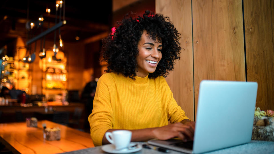 Beautiful smiling African American woman using laptop at the bar.