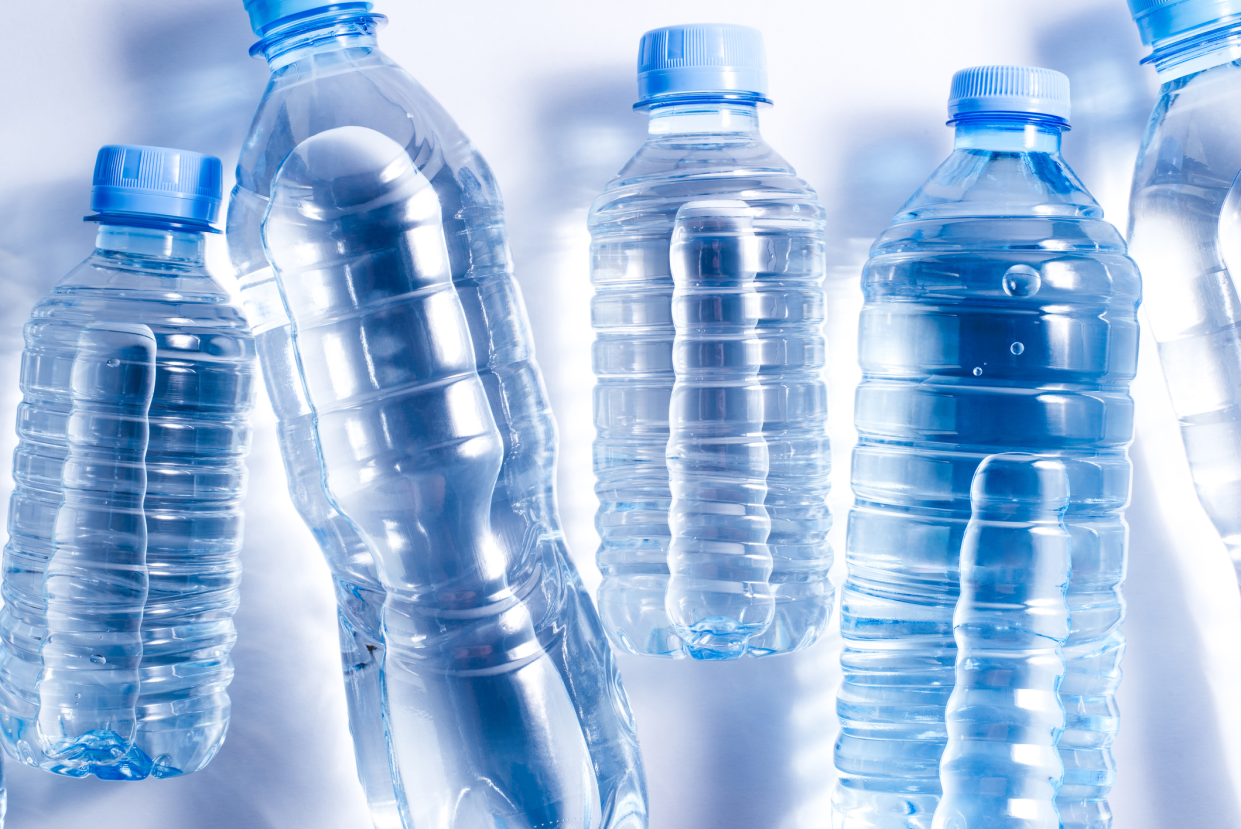 Five plastic bottles of water, different sizes, with shadow of bottles laid on a white background