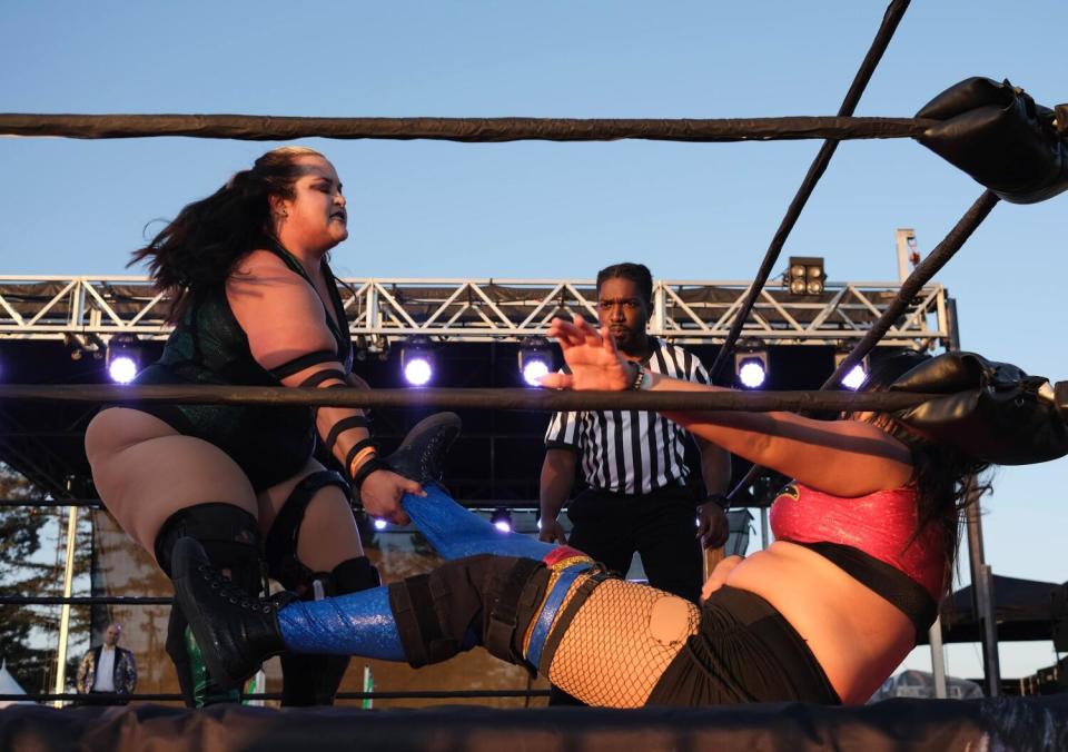 A person grabs the right leg of a person on the floor of a wrestling ring.