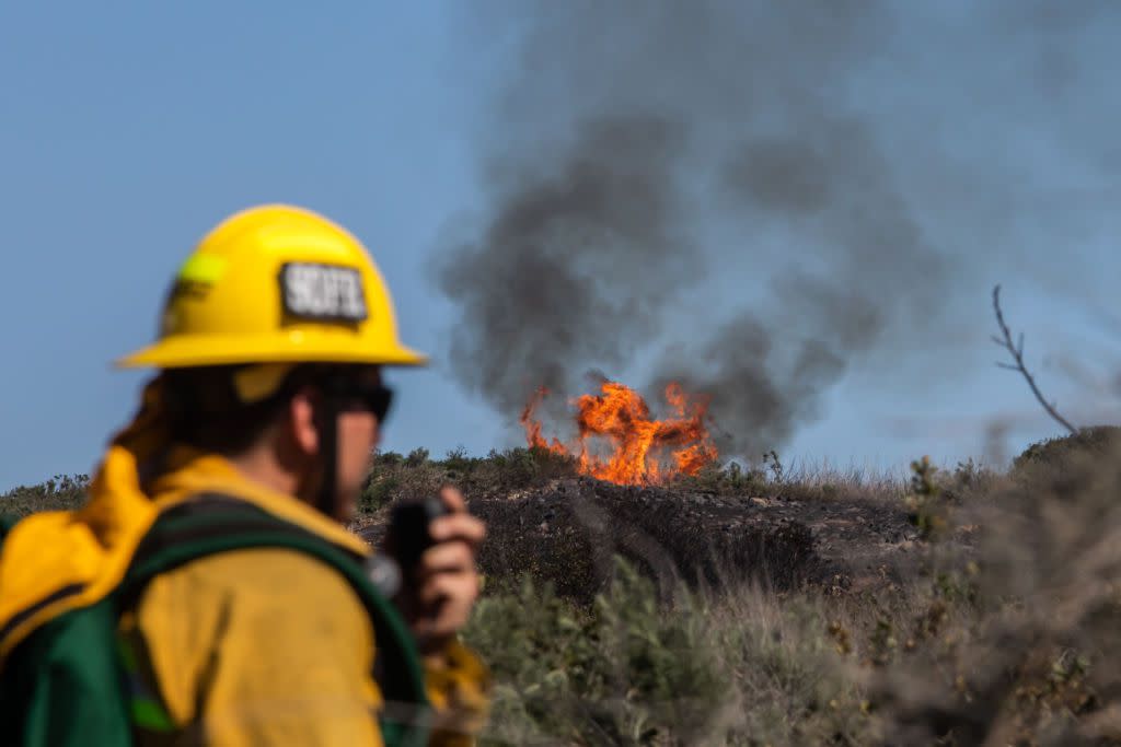 A firefighter talks on the radio while he watches a fire spot on a smoldering hillside on February 10, 2022 in Laguna Beach, California. A wind-driven brush fire that broke out in the hills near Laguna Beach amid high temperatures.