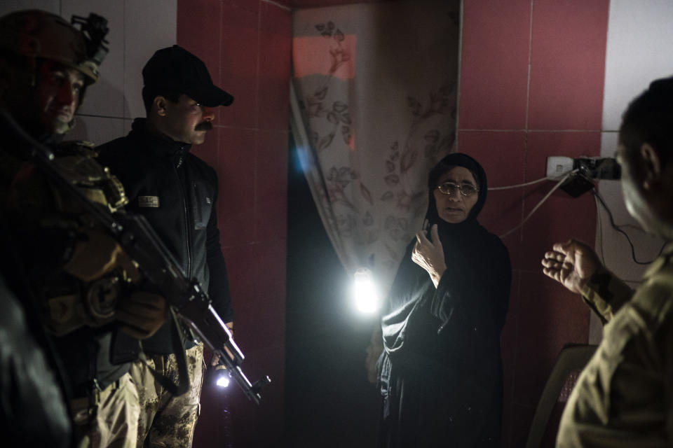 In this April 2, 2019 photo, Iraqi army 20th division soldiers talk to a woman during a nighttime raid near Badoush, Iraq. In towns around the north, Iraqi soldiers knock on doors in the middle of the night, looking for Islamic State suspects, based on intelligence tips or suspicious movements. They search houses and pull people away for questioning. (AP Photo/Felipe Dana)