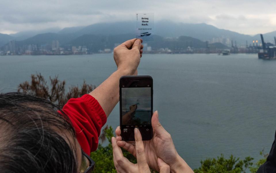 Family members of some of the 12 Hong Kong people detained in mainland China take a photograph of a plastic card reading "Bring Them Back" against a backdrop of Shenzhen - Billy H.C. Kwok /Bloomberg