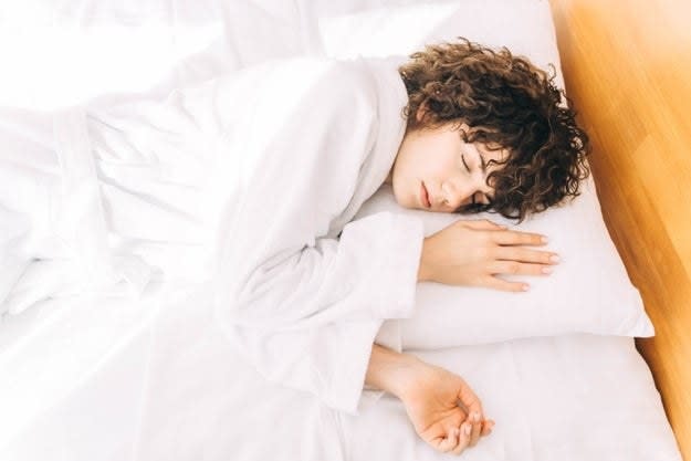 Cheerful woman in a white terry bathrobe is sleeping on the bed in the morning in a hotel