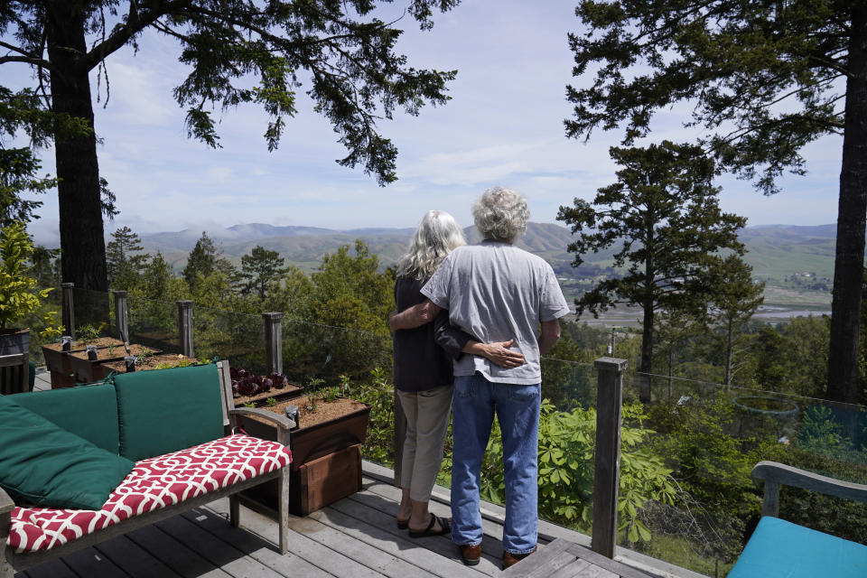 Gordon Bennett and his wife Kate Carolan stand on the deck outside their home and look at the view, Friday, April 30, 2021, in Inverness, Calif. The couple, who were victims of Bernard Madoff and forced to sell their home, now rent it back from someone they know who purchased it. More than 12 years after Madoff confessed to running the biggest financial fraud in Wall Street history, a team of lawyers is still at work on a sprawling effort to recover money for the thousands of victims of his scam. (AP Photo/Eric Risberg)