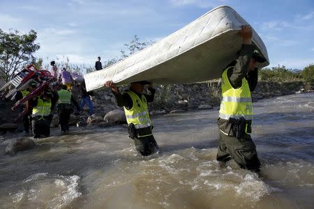 Colombian policemen carry a mattress as they help people to cross with their belongings to Colombia, through the Tachira River at San Antonio in Tachira state, Venezuela, August 27, 2015. REUTERS/Carlos Garcia Rawlins