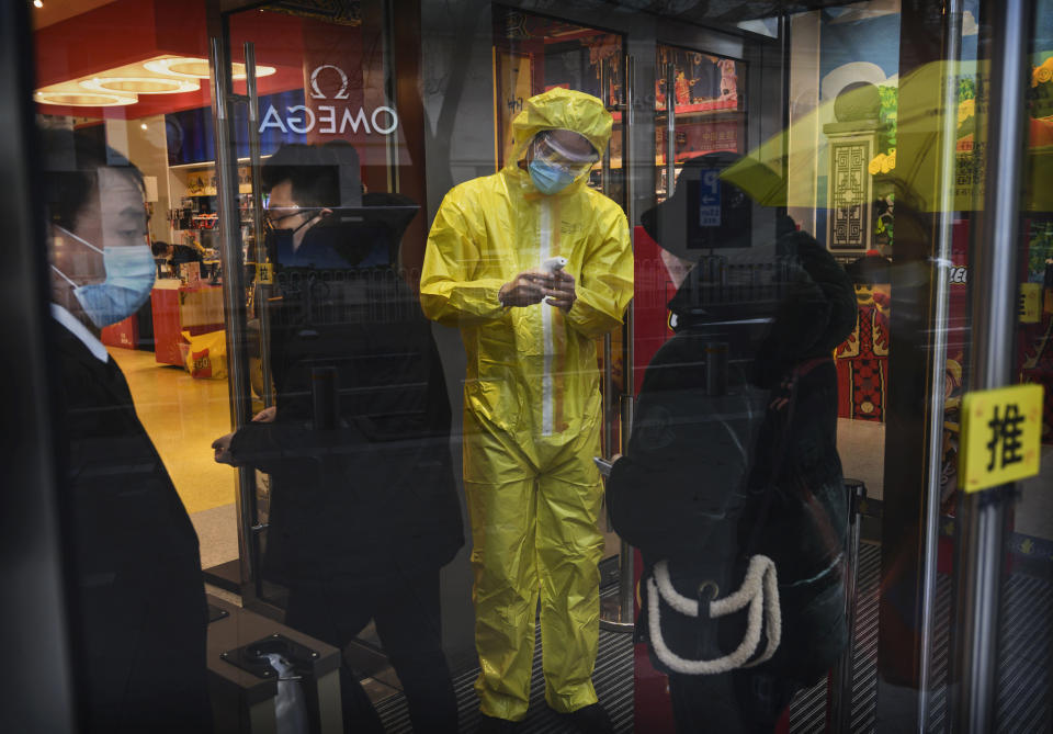 A Chinese worker wears a protective mask suit as he checks customers temperatures in in a shopping area in Beijing, China. 