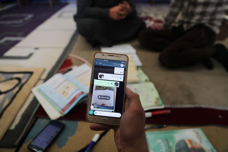 Ahmed Hadaja, a 21-year-old medic and volunteer Arabic teacher, uses his mobile phone to send video lessons and homework to students in Atmeh camp