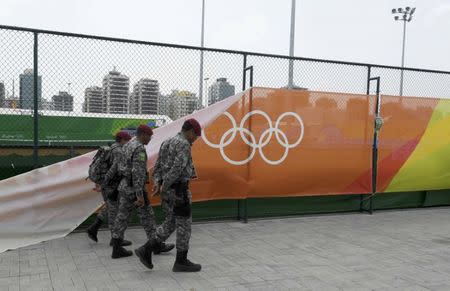 2016 Rio Olympics - Tennis - Olympic Tennis Centre - Rio de Janeiro, Brazil - 07/08/2016. Soldiers walk past a wind damaged banner outside the courts. REUTERS/Toby Melville